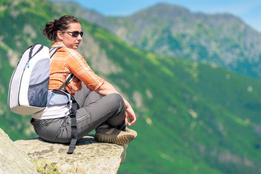 woman sits on a rock in the mountains with a backpack, relax with beautiful scenery