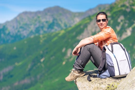 active tourist sits on a rock in the mountains with a backpack, relax with a view of the mountains