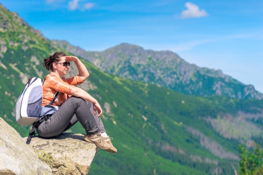 the tourist on the stone sits relax and looks away into the mountains