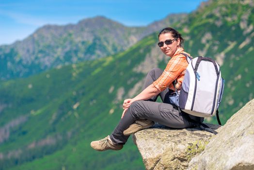 woman hiker with a backpack in the mountains sits on a rock