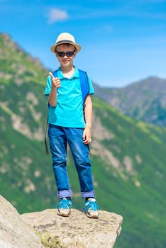 vertical portrait of a happy little traveler with a backpack on the background of mountains