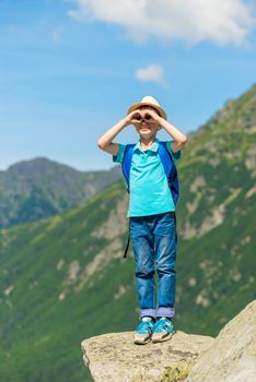 traveler boy looks at beautiful mountains, stands on stone