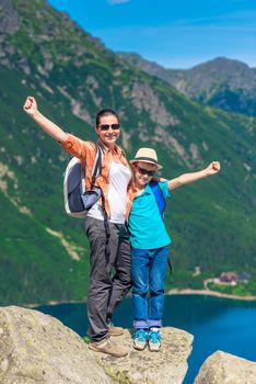 happy mother and son with backpacks high in the mountains against the backdrop of Lake Morskie Oko, Poland