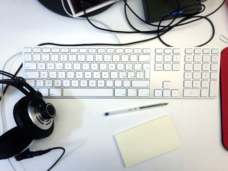 White workspace desk with a computer keyboard, a pen, a note and headphones