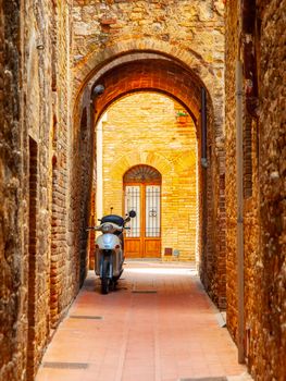 Old medieval street of San Gimignano with small motorcycle, Tuscany, Italia.