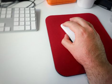 Male hand using a white computer mouse and a red mouse pad