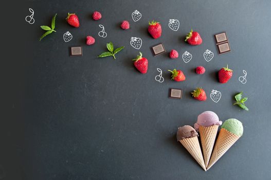 Chocolate, strawberry and vanilla ice cream cones on a chalkboard with a spread of natural ingredients 