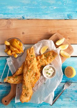 Two pieces of fried fish in batter with chips in a serving basket 