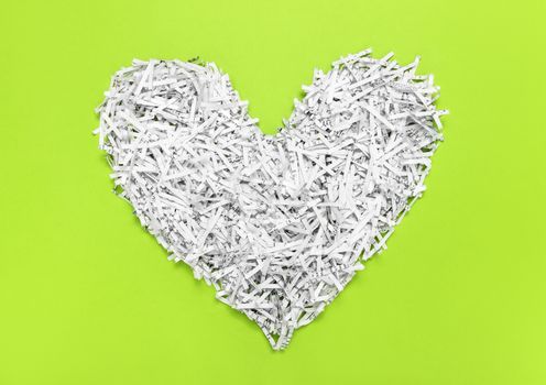 Heart made of shredded paper, on bright green background. Recycling concept.