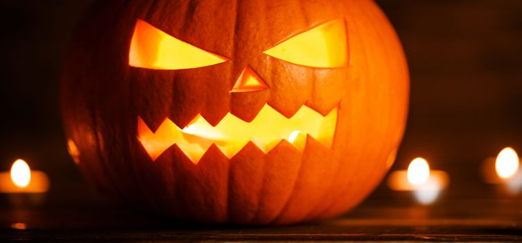 Halloween pumpkin head jack lantern and candles on wooden background