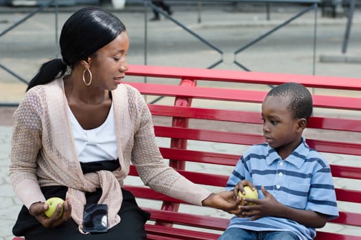 young woman sitting on a bench with her child sharing the apples to eat them.