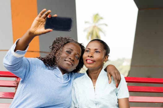 These young women sitting on a bench are photographed with a cell phone.