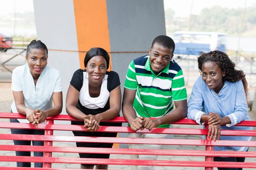This group of young friends in a park leaning on a bench with a beautiful smile.