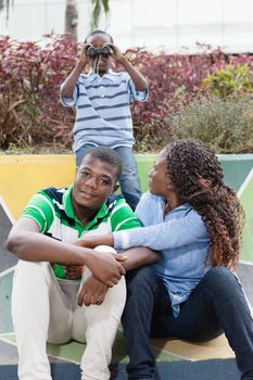 Two young people sitting and behind them a child looking through binoculars.