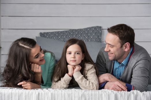 Family portrait of happy parents and their daughter laying on bed at home