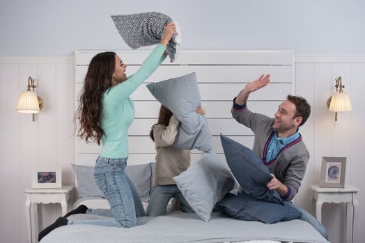 People, family concept - happy child with parents having pillow fight in bed at home