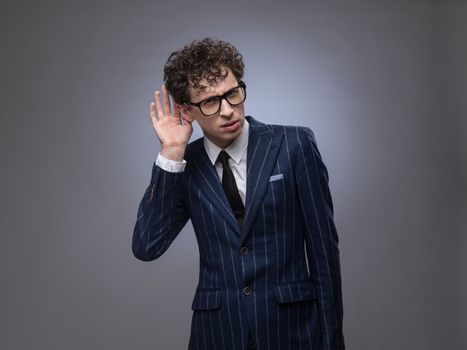 Young man cupping hand behind ear on gray background with copy space - what? cant hear you concept