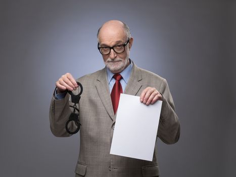 Senior business man with handcuffs and blank contract paper hints at danger of financial crimes