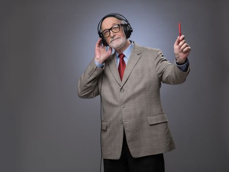 Portrait of senior man in headphones listening music, studio shot on gray background