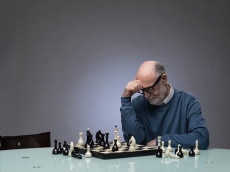 Senior man thinking over his move in chess, studio shot on gray background with copy space