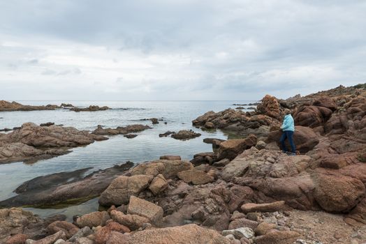 Valdorama,Italy,11-april-2018:Adult woman sitting on the rocks of isola rossa the read coast of sardinia island belongs to italy,sardina has the most beautifull coastline