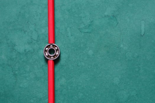 One ball bearing between two red pencils on green background