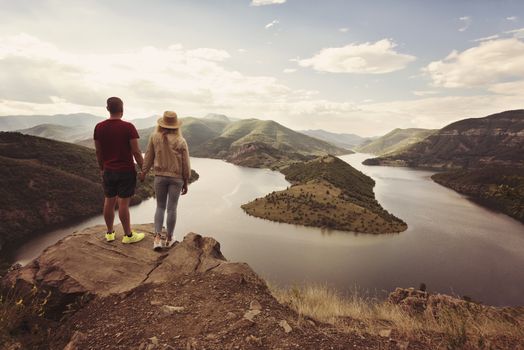 Hiking couple looking at the view holding hands. Location: the meanders of Arda river, Bulgaria.