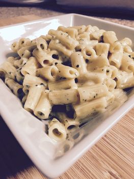 Hot and fresh vegetarian pasta with broccoli on white square plate.