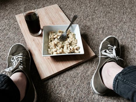 Tasty and fresh broccoli pasta on the floor at home near man legs.