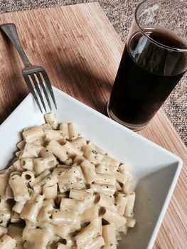 Delicious and fresh pasta on wooden board near black coke in glass.