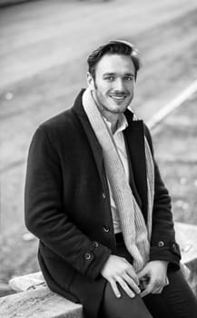 Handsome young man outdoor in winter fashion, wearing black coat and woolen scarf in city park