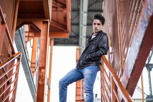 Handsome young man standing outdoors in urban environment on metal stairs, looking at camera