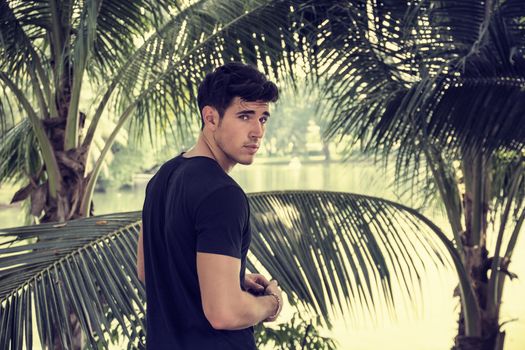 Attractive young man outdoor in nature, near palm trees in a sunny day