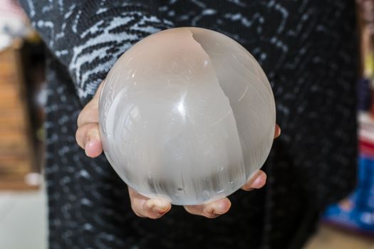 Close up shot of crop female hands holding sphere made of selenite or white quartz.