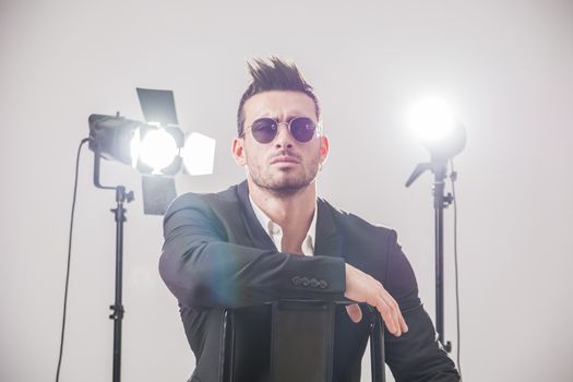 Handsome man in stylish suit and sunglasses posing in studio lights.