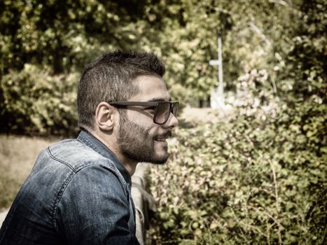 Handsome young man at countryside, in front of field or grassland, wearing shirt, looking away to a side