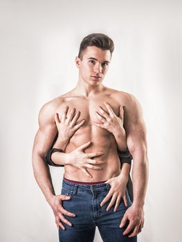 Shirtless, fit young man and four female hands touching him from behind, on white