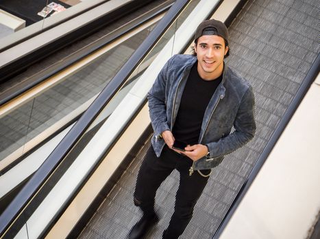 Young trendy man on moving walkway or travellator or autowalk, looking ata camera