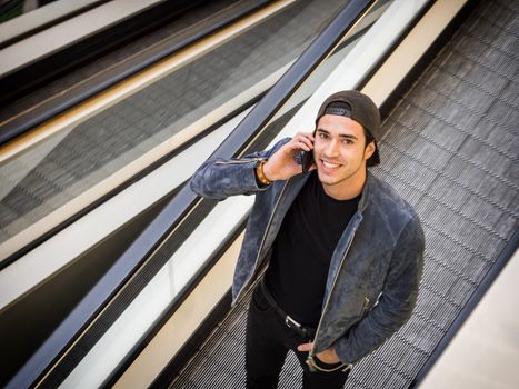 Young trendy man on moving walkway or travellator or autowalk, looking ata camera