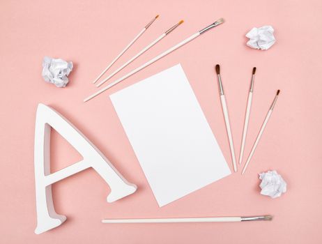 Arts and creativity. Letter A, paintbrushes and blank paper, on pastel pink background.