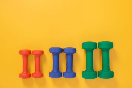 Dumbbells of different colors and sizes, on joyful yellow background with copy space.