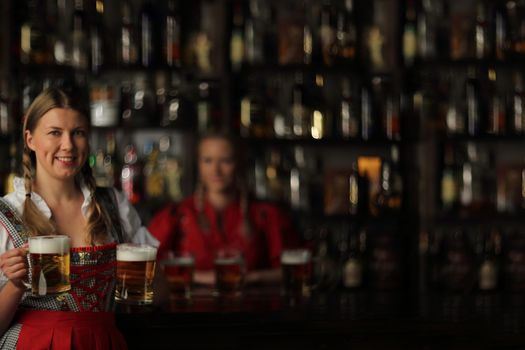 Pretty oktoberfest blonde woman holding beer mugs in bar