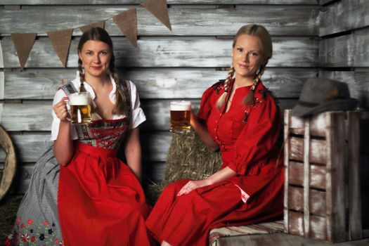 Beautiful Oktoberfest women holding beer mugs on hay
