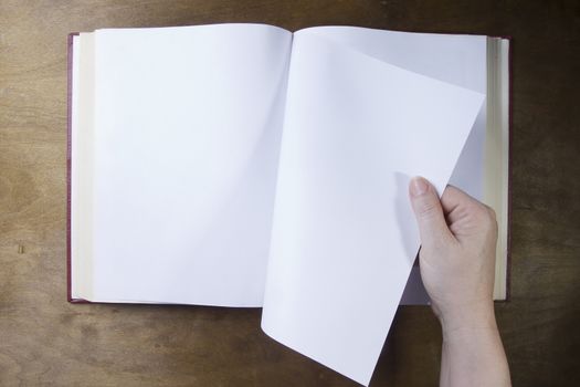 Hand turns the blank sheet of books on a wooden table