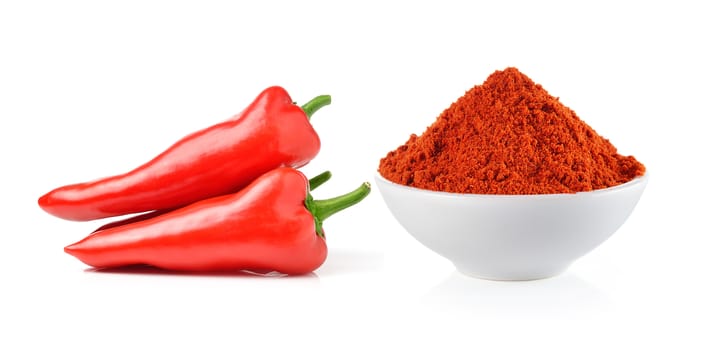 Powdered dried red pepper and red chili peppers in a white bowl on white background