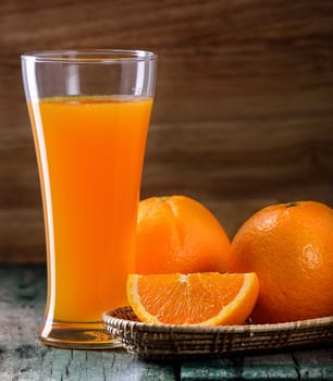 Orange juice glass and fresh oranges on wood