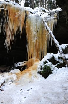 Frozen waterfalls on the rock, orange colored and snow