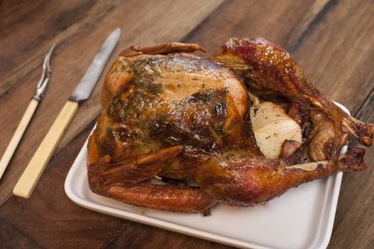 Close-up of deep fried whole chicken on pan with knife and fork on wooden table