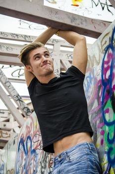 Attractive blue eyed, blond young man in black t-shirt hanging from concrete structure