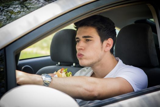 Young handsome man driving his car while eating food in the traffic